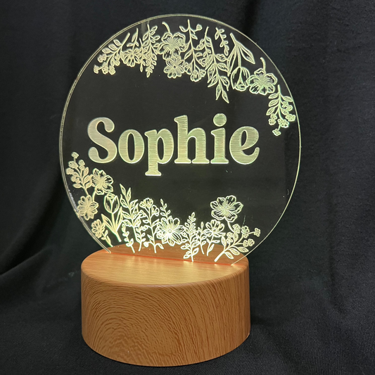 Personalized Wildflower Name Night Light featuring laser-engraved wildflowers surrounding a custom name on a clear acrylic panel, softly illuminated by an LED light on a wooden base