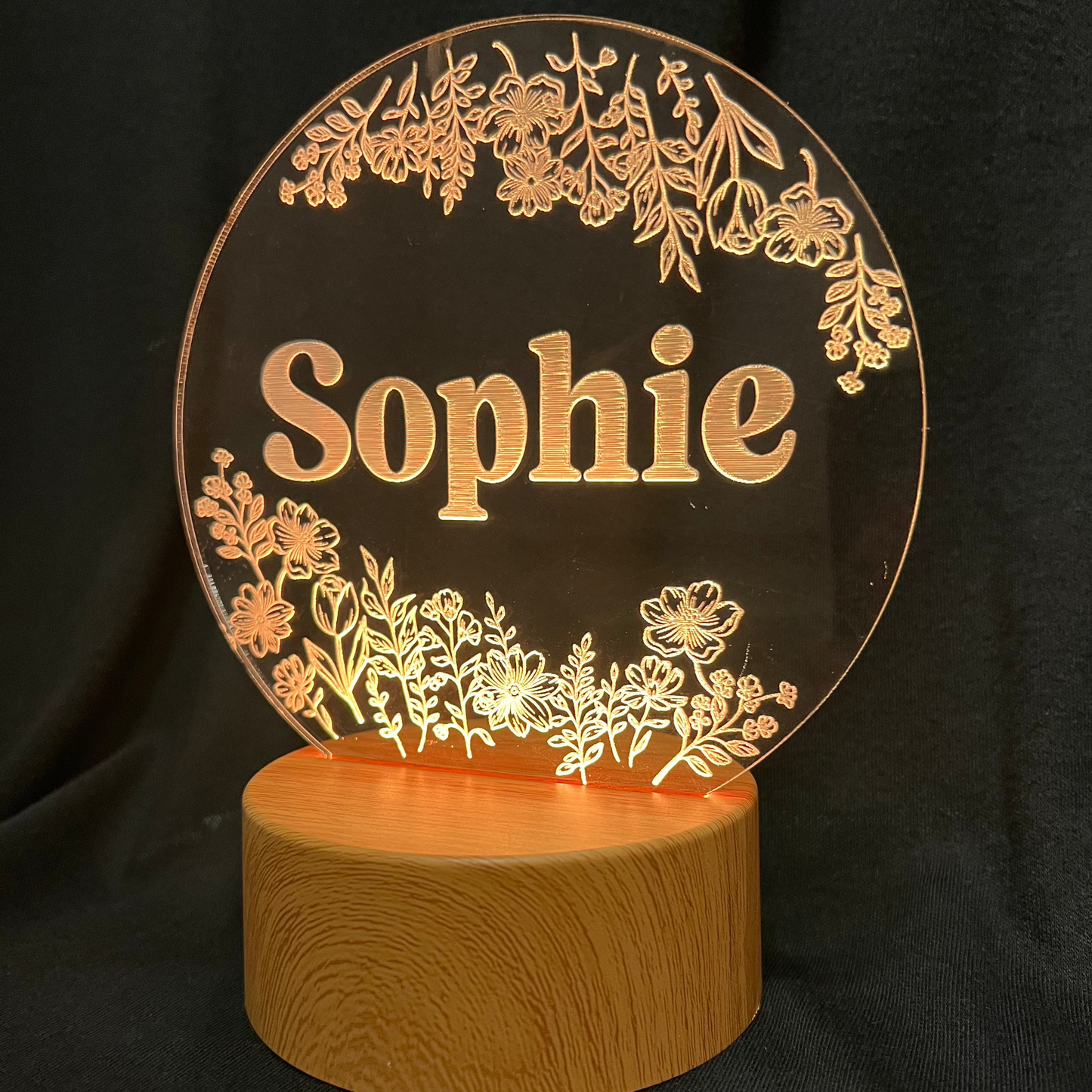 Personalized Wildflower Name Night Light featuring laser-engraved wildflowers surrounding a custom name on a clear acrylic panel, softly illuminated by an LED light on a wooden base