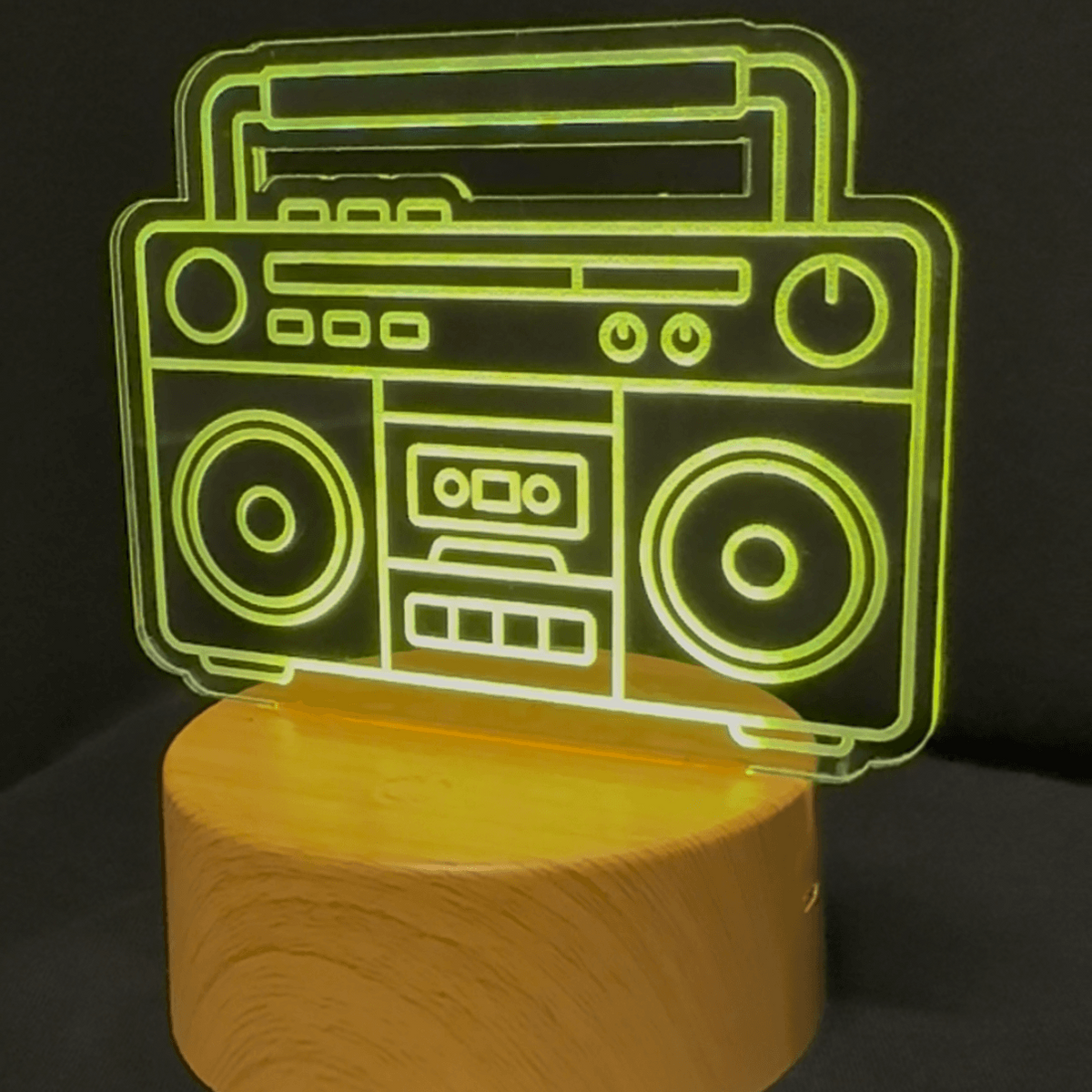 A retro-style boombox-shaped LED night light with a glowing green outline, mounted on a cylindrical wooden base against a dark background.