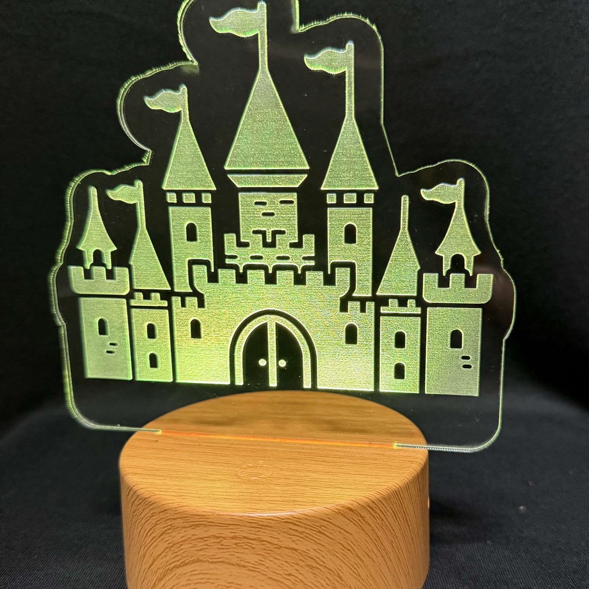 A wooden cylindrical base supporting a clear acrylic castle-shaped light or plaque, photographed against a dark fabric background.