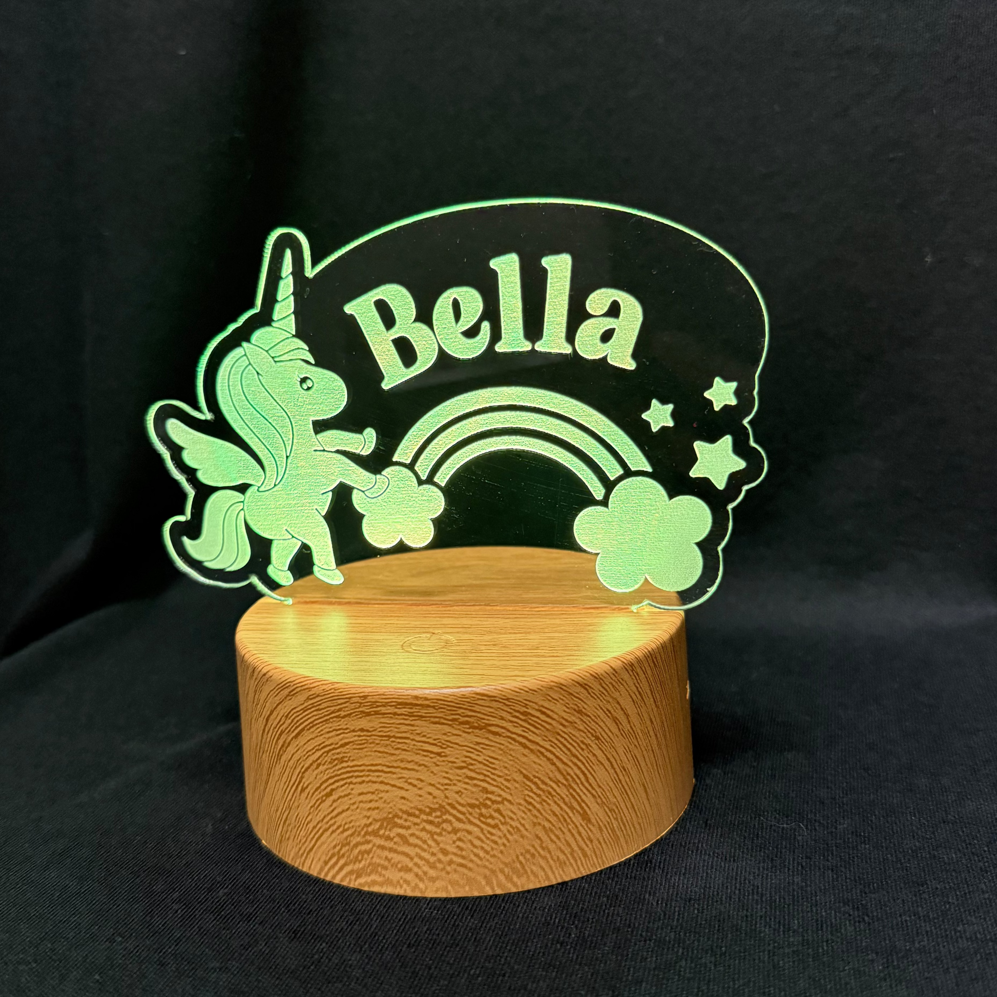 Decorative sign with unicorn, rainbow, and flowers on a wooden base against a black background